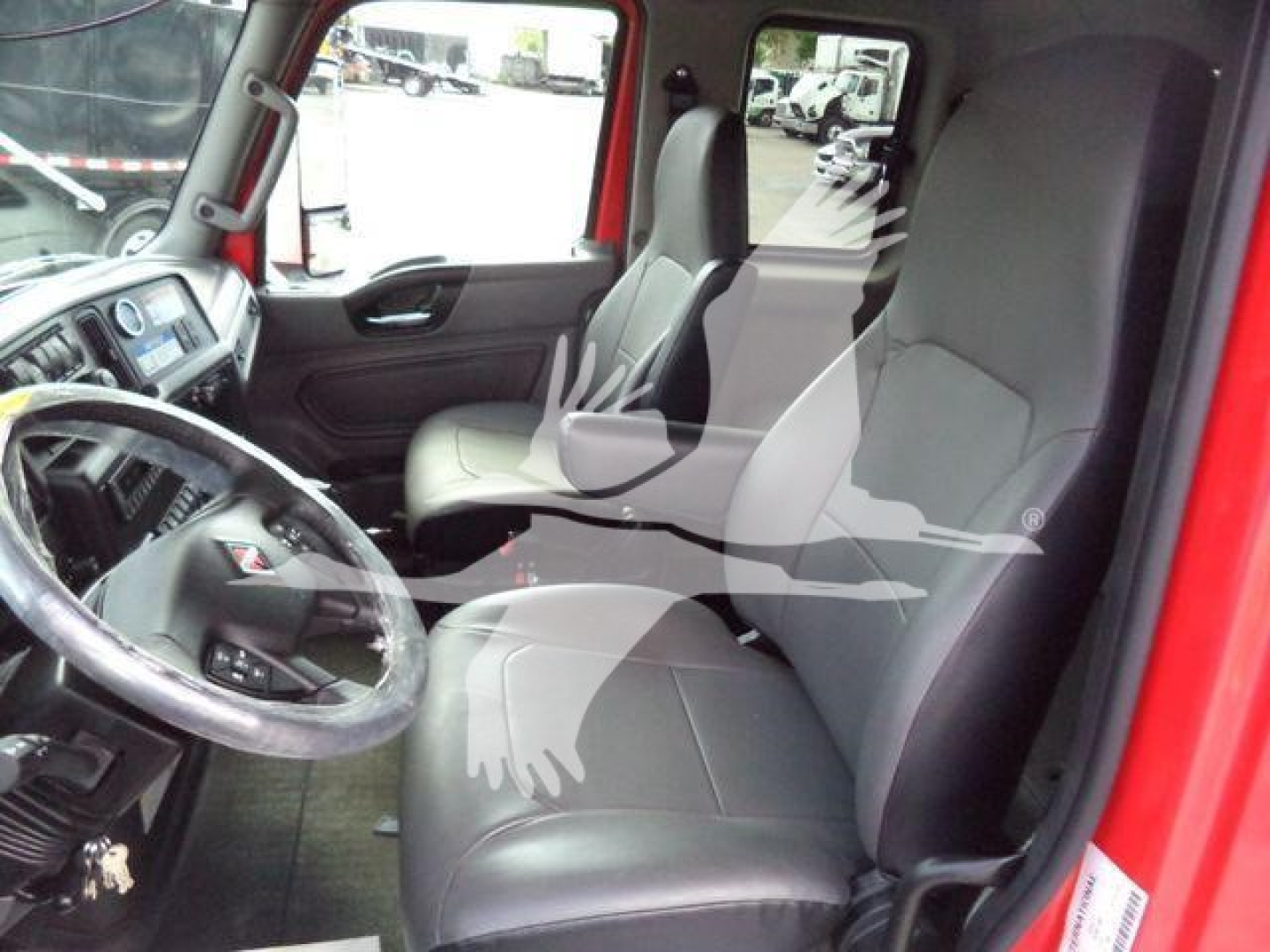 Interior of a truck cab showing driver seat and passenger seat with steering wheel and dashboard visible in a red International MV truck.
