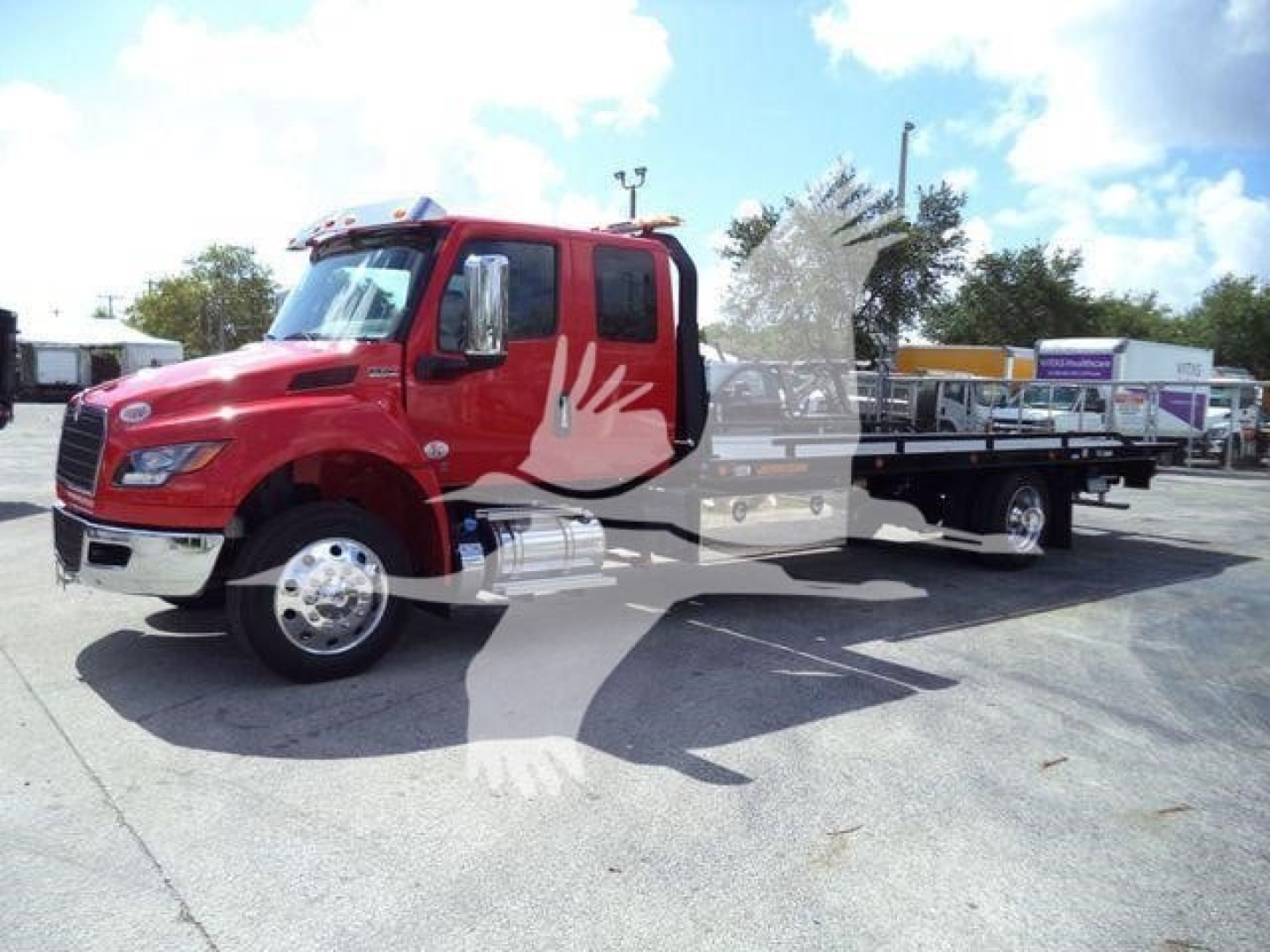 Red International MV rollback tow truck with flatbed, front grille, dual large side mirrors, and chrome exhaust stack visible.