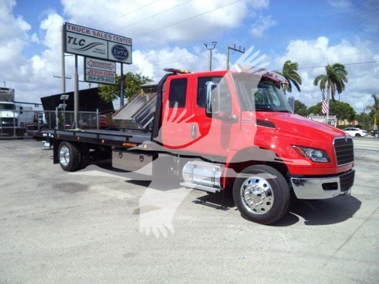 Red International MV rollback truck with flatbed, side view showing cab and chrome bumper; dealership lot in background with palm trees and sign.