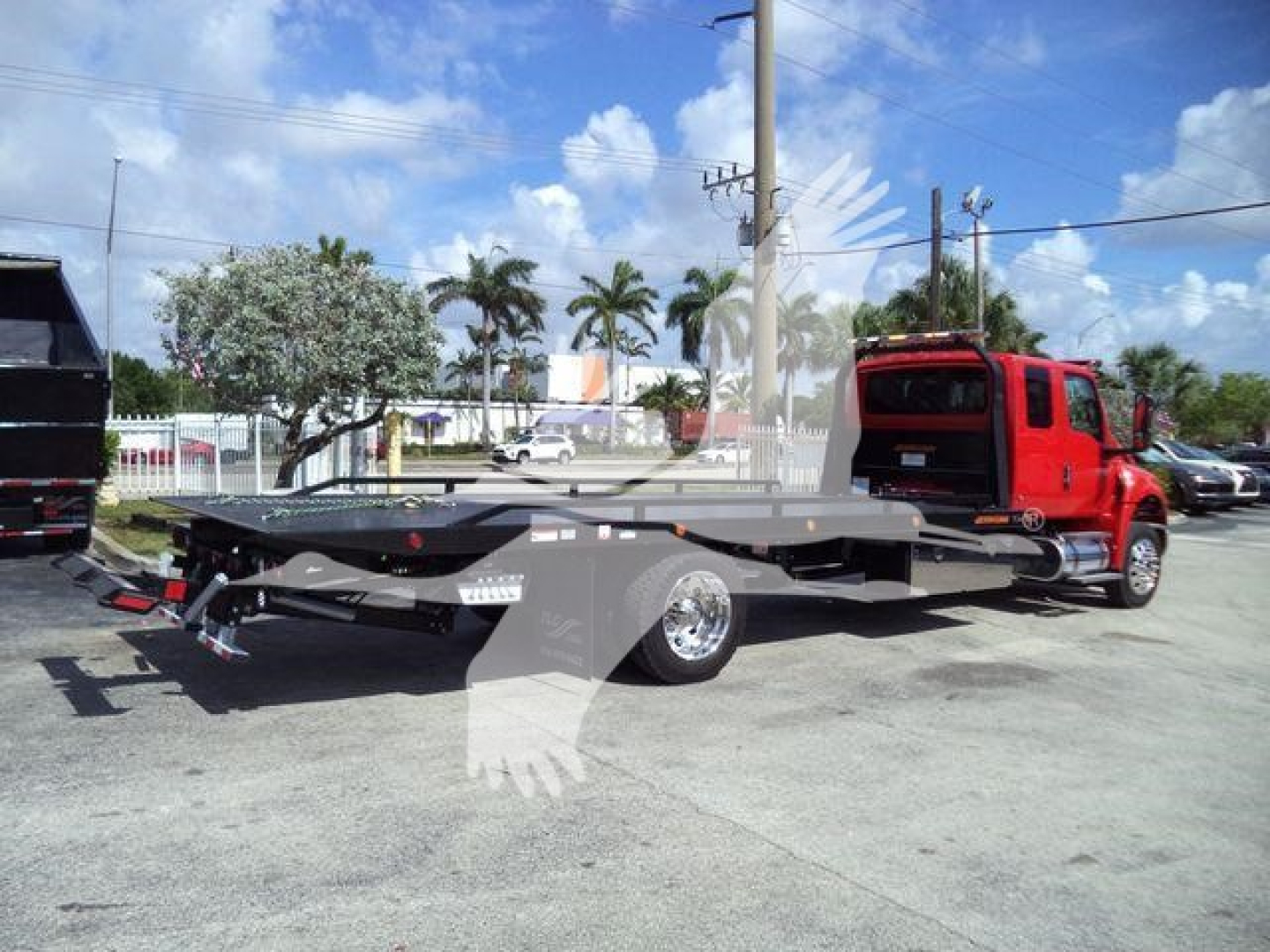 MV-series truck in service bay showing a rollback tow truck with a low flatbed and red cab, side view with hydraulic winch and rear equipment.