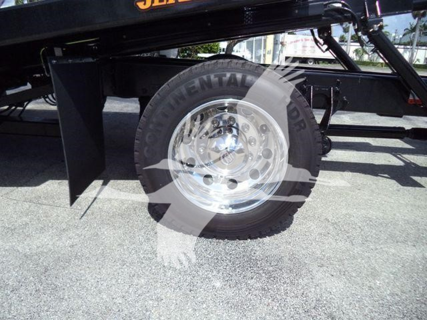 Truck component close-up showing a single wheel and suspension of a 2027 International MV rollback truck with polished aluminum rim and tire, partial frame, and black undercarriage.