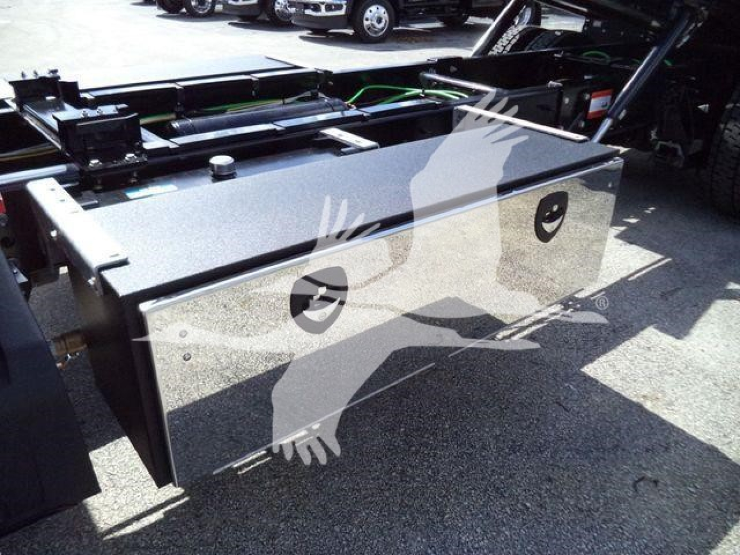 Toolbox/storage box mounted on a truck chassis, reflective metal surface with two circular black access ports, viewed in a truck yard.