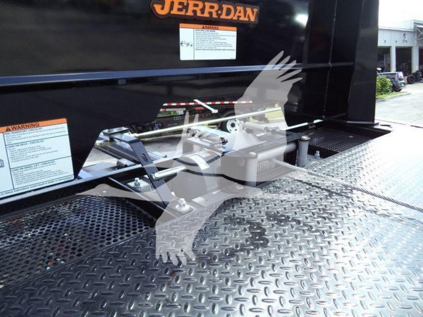 Truck bed platform with attachment hitch and metal diamond-plate surface; stickered labels and 'JERR-DAN' logo on the side of a rollback truck.