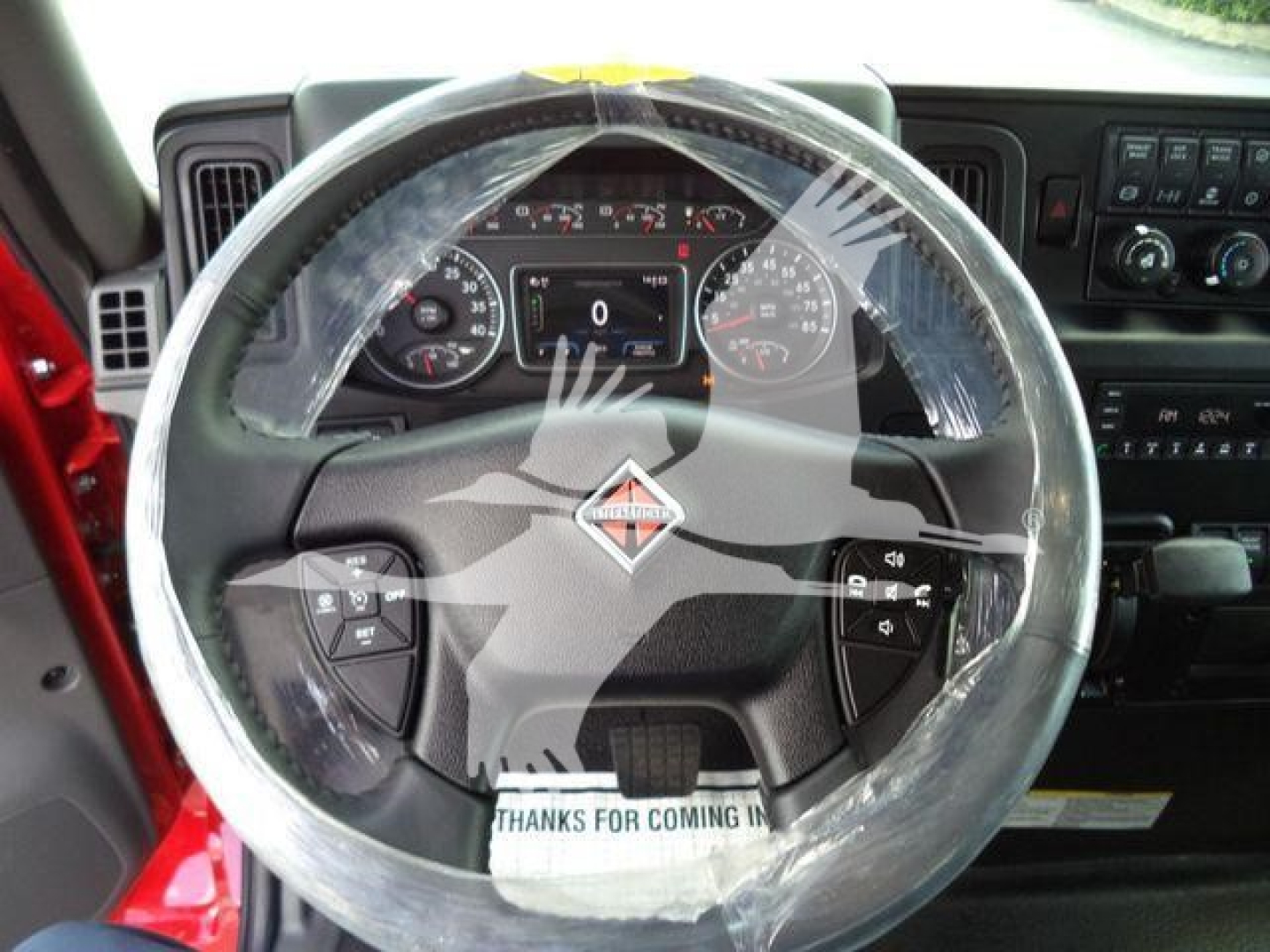 Truck steering wheel in the cab with plastic wrap, dashboard gauges, and controls visible; brand emblem on the center of the steering wheel.