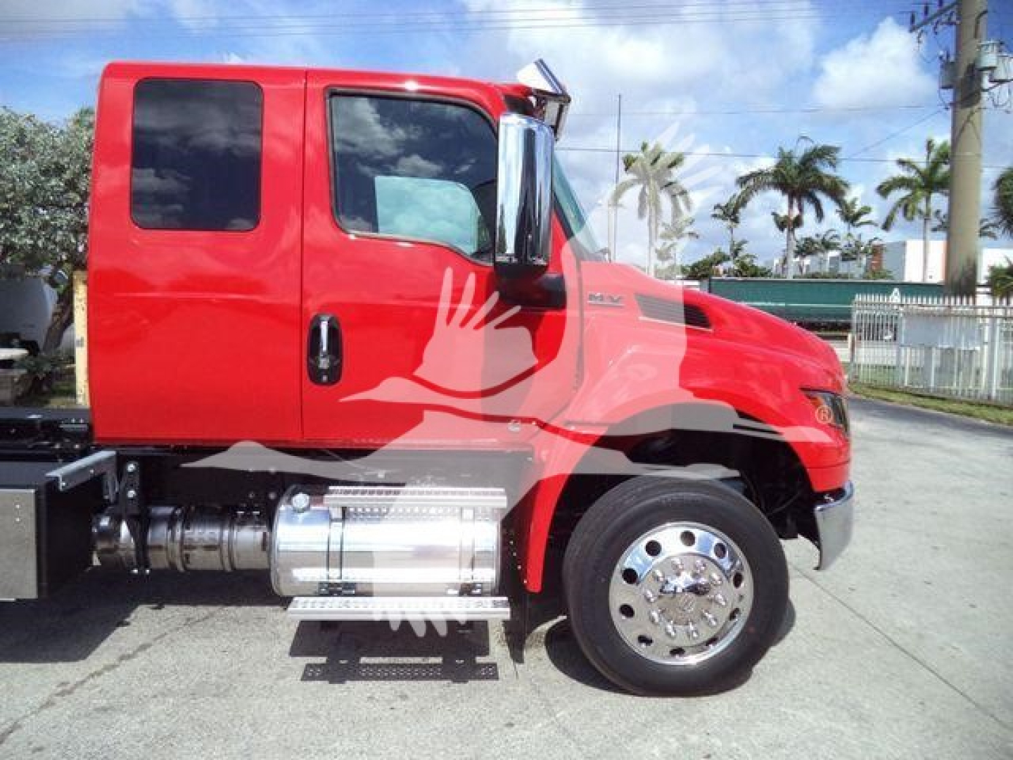 Truck cab side view showing red International MV with chrome fuel tank and step, single rear axle, wheel, and door handle.