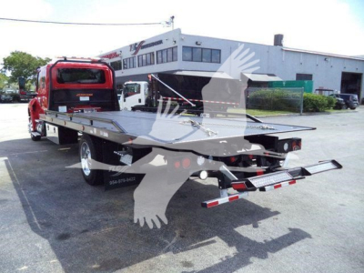 Truck showing a flatbed rollback with red cab and black flatbed, tag numbers visible on side, rear hitch and reflectors.