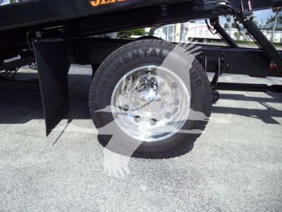 Truck component close-up showing a single wheel and suspension of a 2027 International MV rollback truck with polished aluminum rim and tire, partial frame, and black undercarriage.