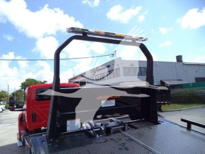 Truck rollback bed with metal diamond plate and a curved black rollover protective frame; red cab in background; warning light bar on top.