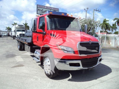 Red International MV rollback truck in a dealership lot showing front cab with chrome bumper, large grille, and extended flatbed.