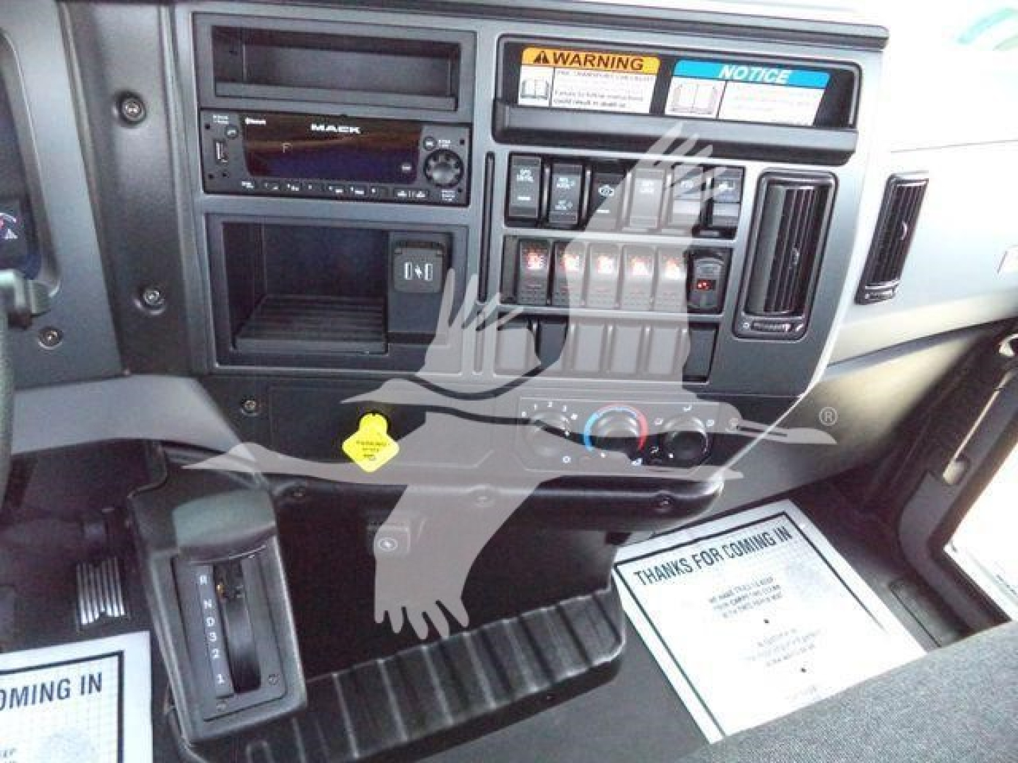 Dashboard interior of a 2025 Mack MD6 truck showing radio, climate controls, warning stickers, and ignition area.