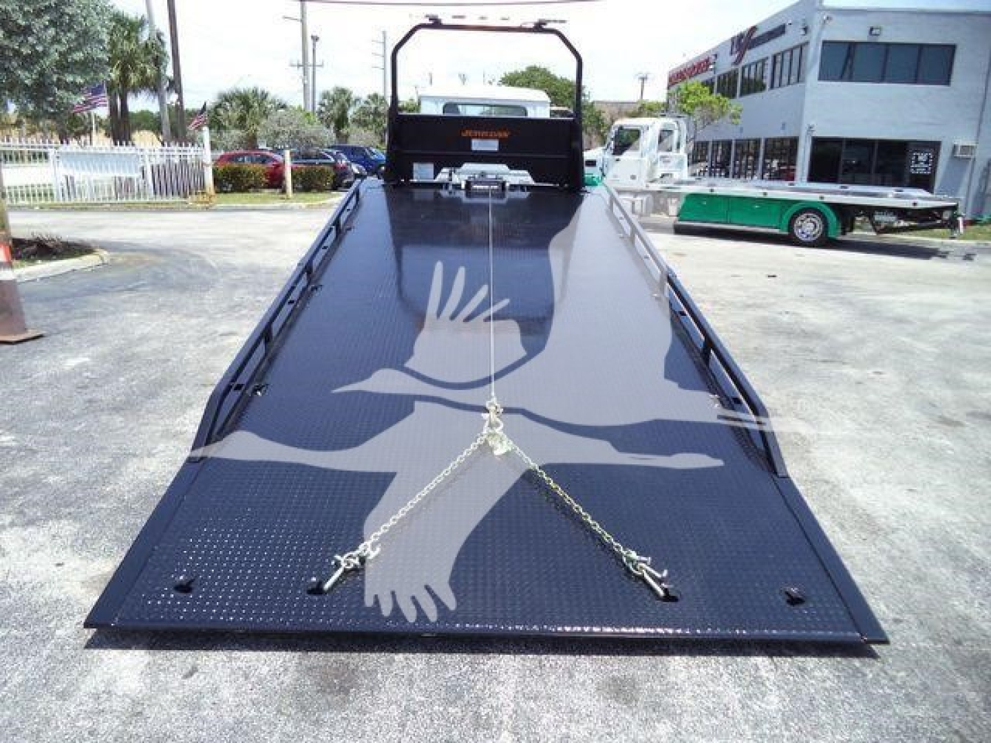 2025 Mack MD6 rollback truck bed/platform with chains, loading ramp, and black textured surface.