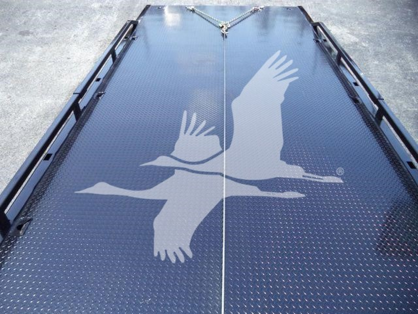Truck roll-back deck with non-slip diamond plate surface and a large white bird graphic, center seam and railings visible along edges.