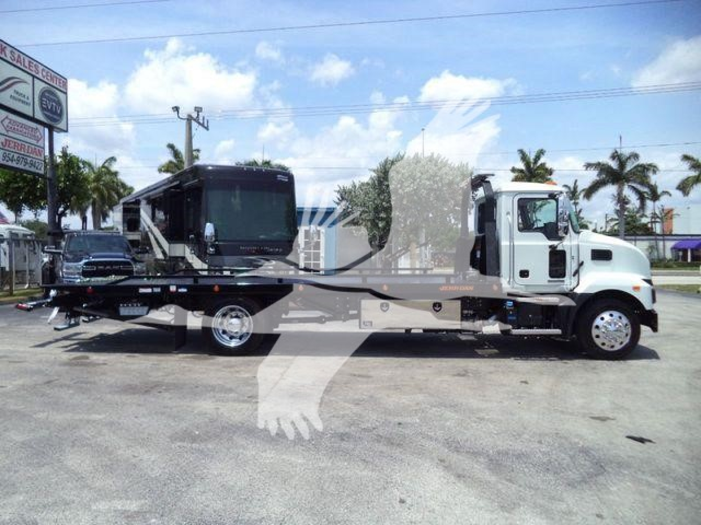 Truck-mounted rollback wrecker on a 2025 Mack MD6 chassis showing a long flatbed and a mounted crane, side view with white cab and grey bed.
