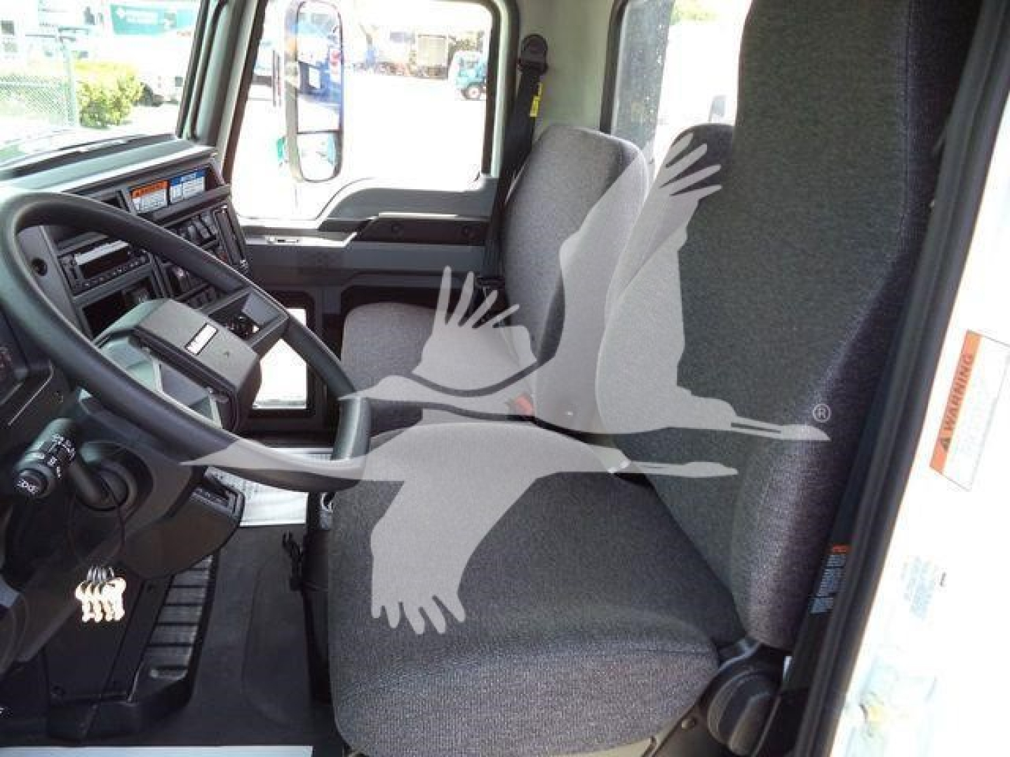 Truck cab interior showing steering wheel, dashboard, driver seat, and passenger seat in a new Mack MD6 rollback truck.
