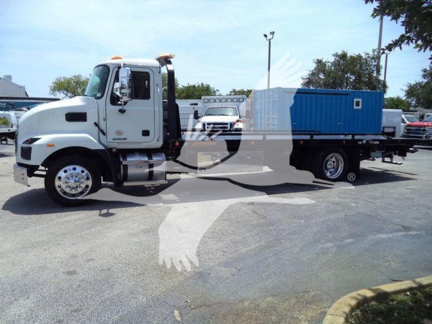 MD6 Mack rollback truck showing a blue equipment container on flatbed with white cab and orange beacon lights
