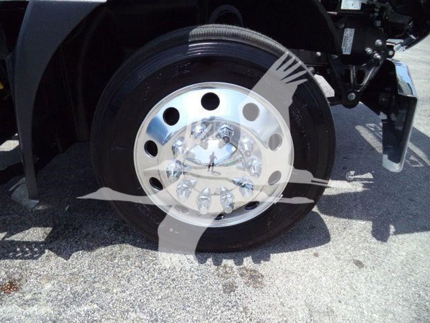 Wheel and front axle of a Mack MD6 rollback truck showing chrome hub and black tire with metal lug nuts.