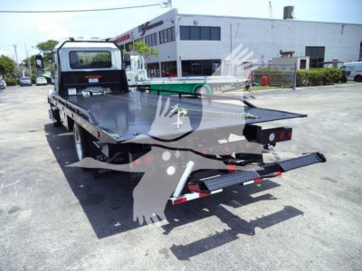 Flatbed tow truck rear view showing blue-gray steel deck and ramp ramps with reflective tape, Mack Md6 chassis, service lot background.