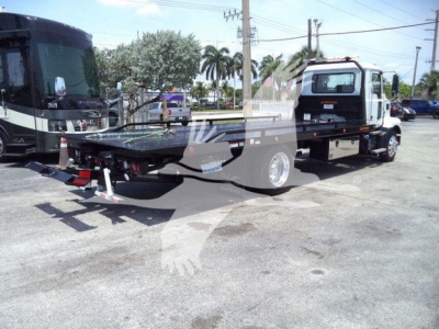 MD6 tow truck chassis showing flatbed with wheel-lift and Mack cab in background.