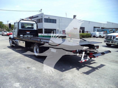 Flatbed tow truck in a parking lot with a Mack MD6 cab and a long flatbed; visible text includes stock number J10538; category Rollback; type Trucks; new/used New.