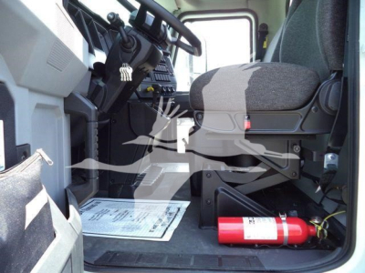 Cab interior of a 2025 Mack MD6 truck showing driver seat, dashboard, pedals, and a red fire extinguisher on the floor near the entry.