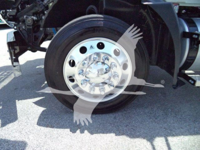 Wheel/tire assembly of a Mack MD6 truck showing polished aluminum wheel with multiple circular holes and hubcap; part of the chassis and fender visible.