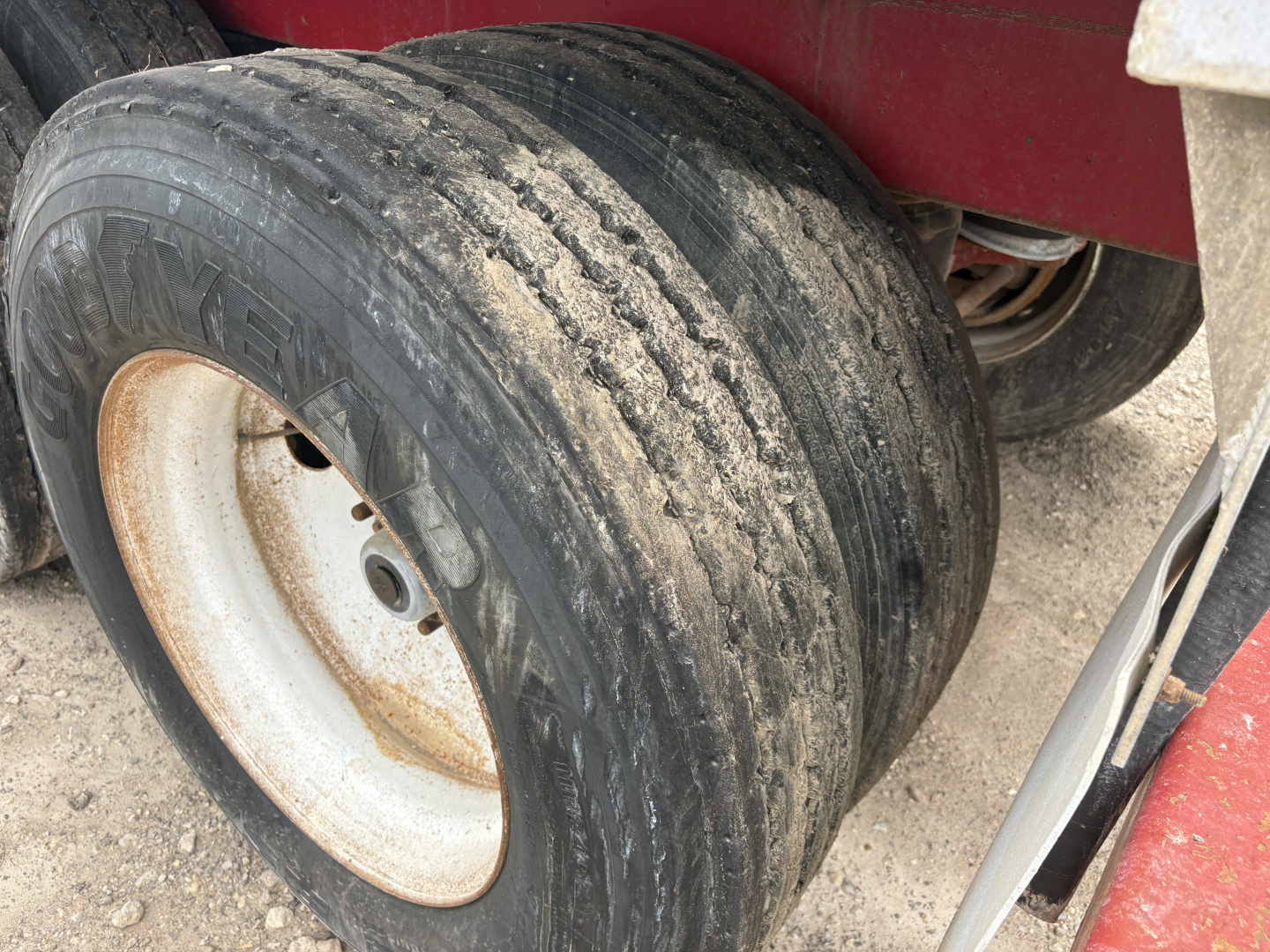Trailer wheel showing worn tire and white rim, dirt and mud on surface.