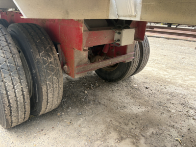 Trailer axle and undercarriage with dual rear tires, red frame and leaf spring suspension, dirt ground.