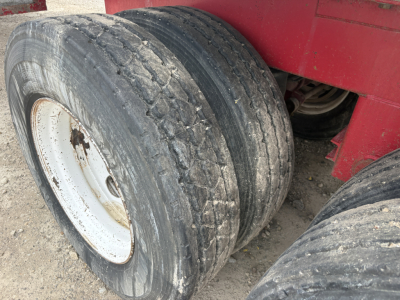 Trailer wheel assembly with dual axles and worn tires on a red trailer, showing the tread and white steel rims.