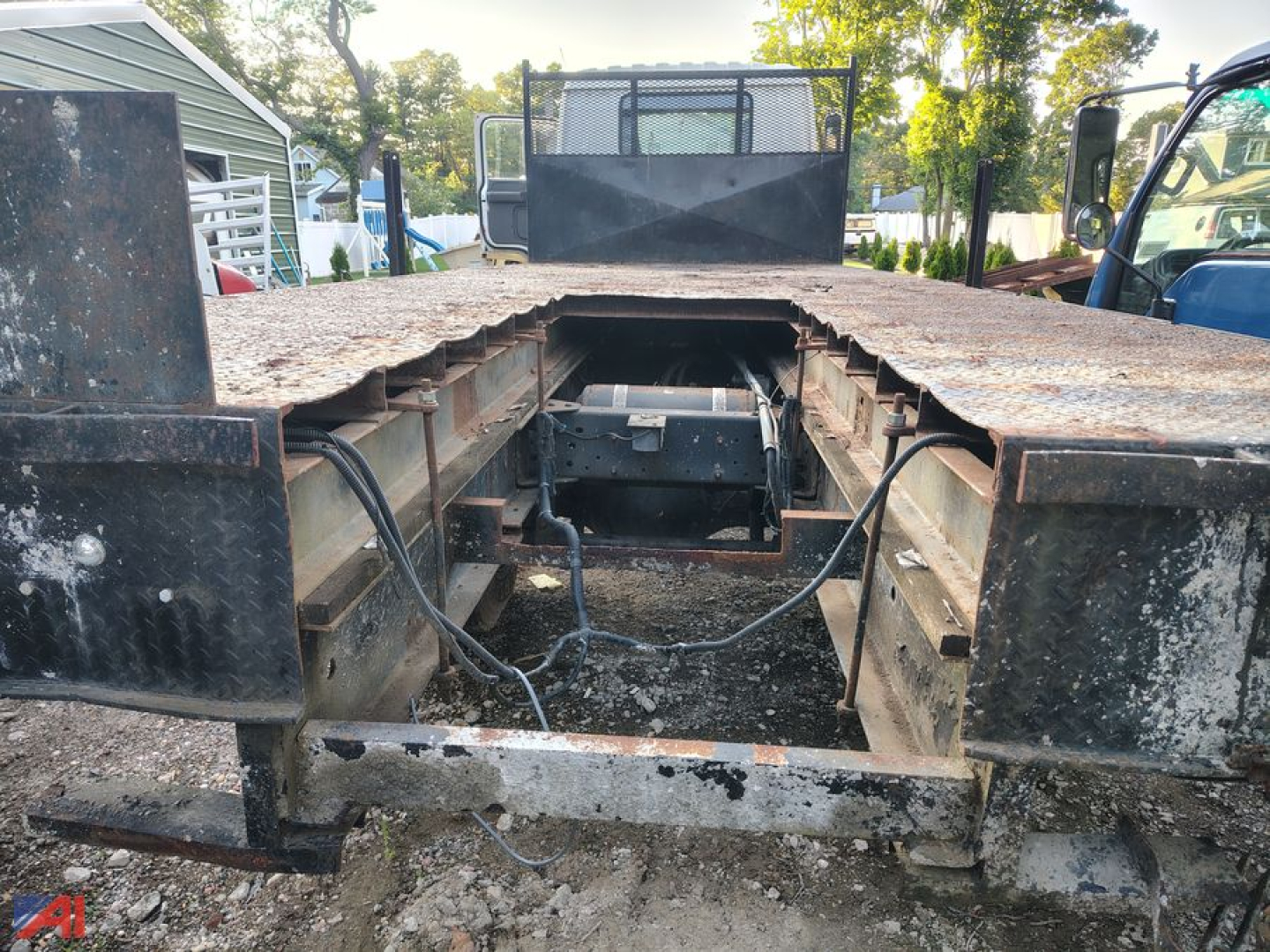 GMC T7500 cab and flatbed showing exposed frame and drivetrain access hatch with rusted metal bed and side rails.