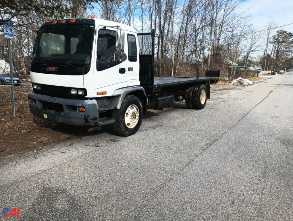 GMC T7500 cab with flatbed truck in a parking lot, white cab, black flatbed, front view