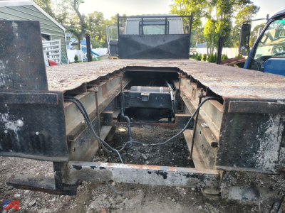 GMC T7500 cab and flatbed showing exposed frame and drivetrain access hatch with rusted metal bed and side rails.