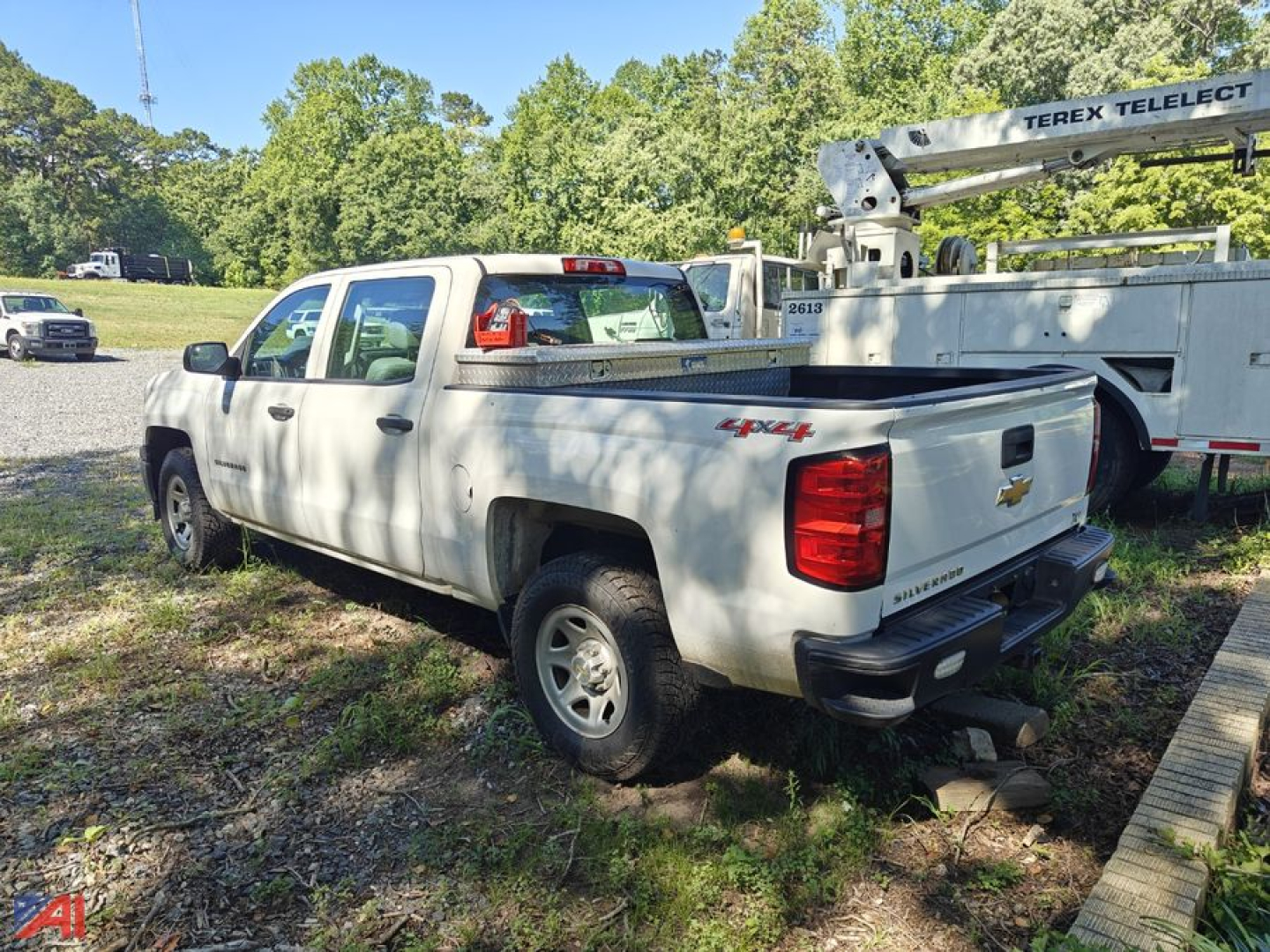 Chevrolet Silverado 1500 pickup truck in a grassy lot, white extended cab with a tonneau cover, rear view showing tailgate and bumper.