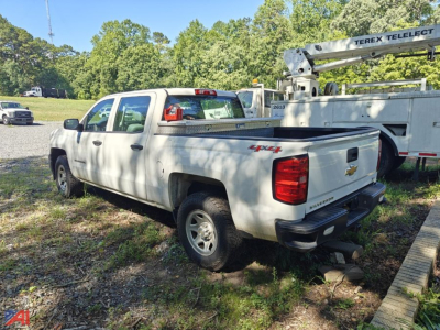 Chevrolet Silverado 1500 pickup truck in a grassy lot, white extended cab with a tonneau cover, rear view showing tailgate and bumper.