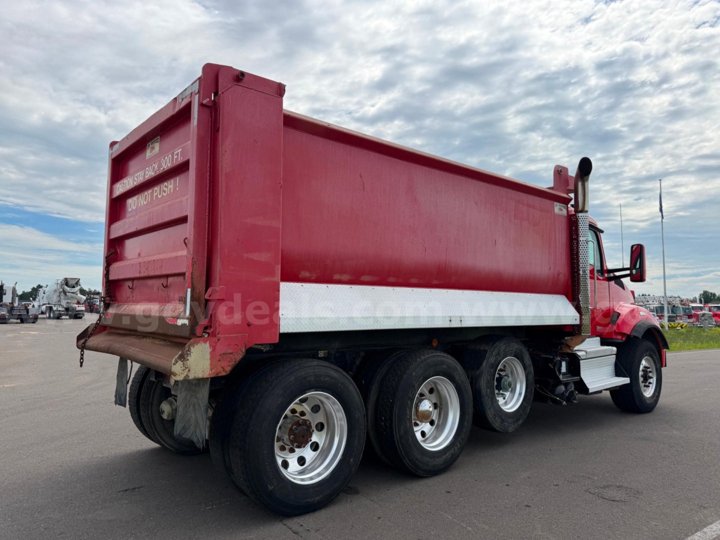 Kenworth T880 dump truck with red dump body and dual rear axles, showing side view of cargo bed and wheels.