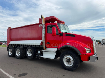 Kenworth T880 dump truck in red, side view with multiple rear axles and dump bed, on a paved lot.