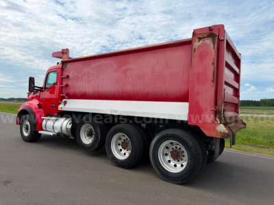 Kenworth T880 dump truck side view showing red dump body and white lower side rail with three rear axles on a road.