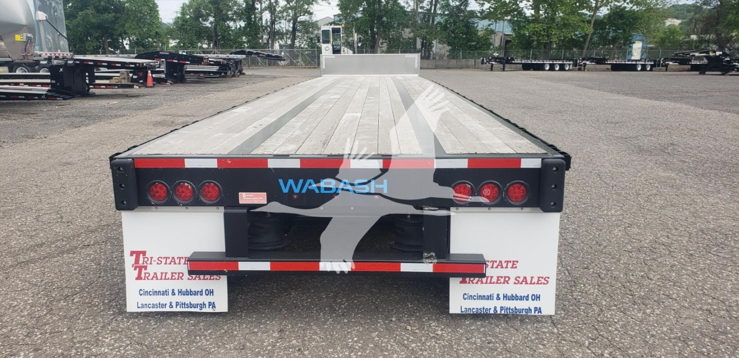Rear view of a used 2024 Wabash steel drop deck trailer showing taillights, white and red reflective tape, WABASH logo, and dealer plates.