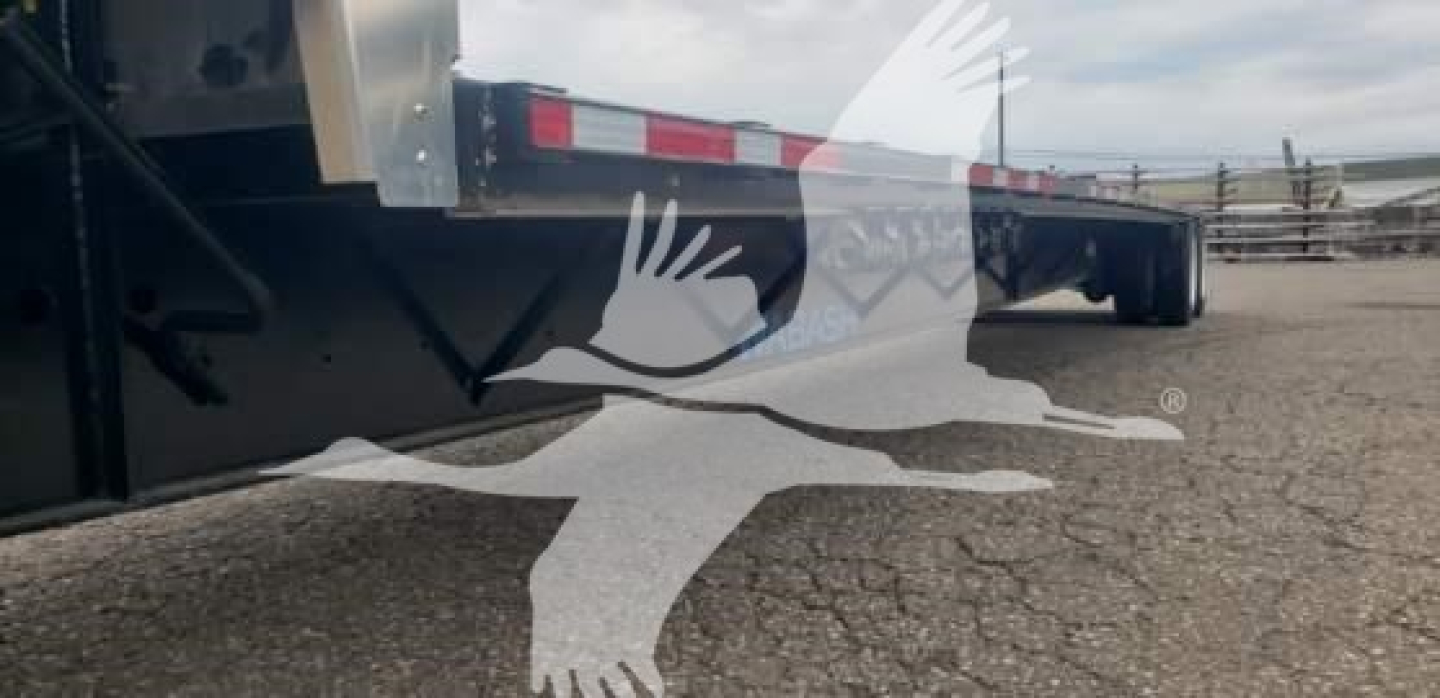Trailer underside and frame of a 2024 Wabash steel drop deck trailer showing deck supports and corner with reflective tape.