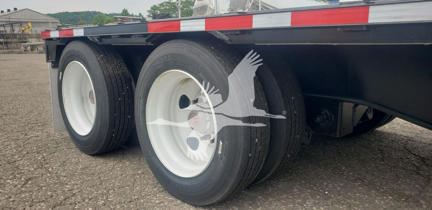 Wheel ends of a Wabash steel drop trailer showing dual rear axles and white rims with black tires.