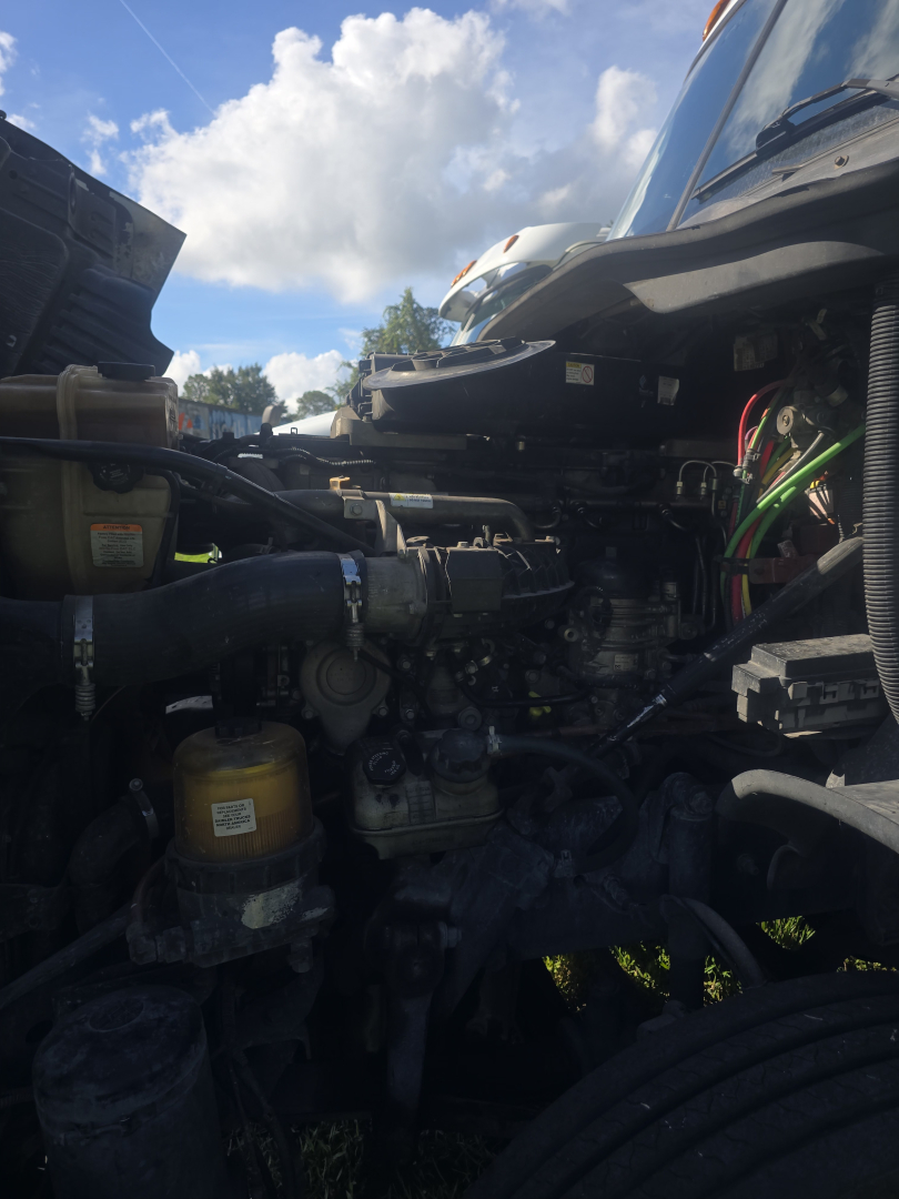 View of a truck engine bay with various hoses, reservoirs, and components; visible labels include a yellow fuel filter canister and various hoses; parts and wiring are in view.
