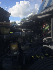 View of a truck engine bay with various hoses, reservoirs, and components; visible labels include a yellow fuel filter canister and various hoses; parts and wiring are in view.