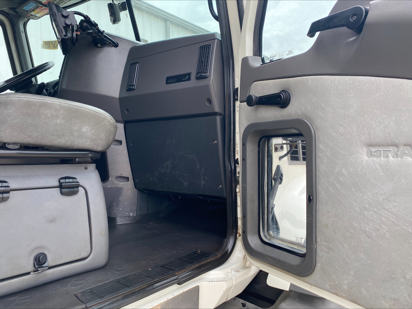 Cab interior of a 2018 Mack GU533 roll-off truck showing front passenger door open and driver seat area with dashboard and center console visible.