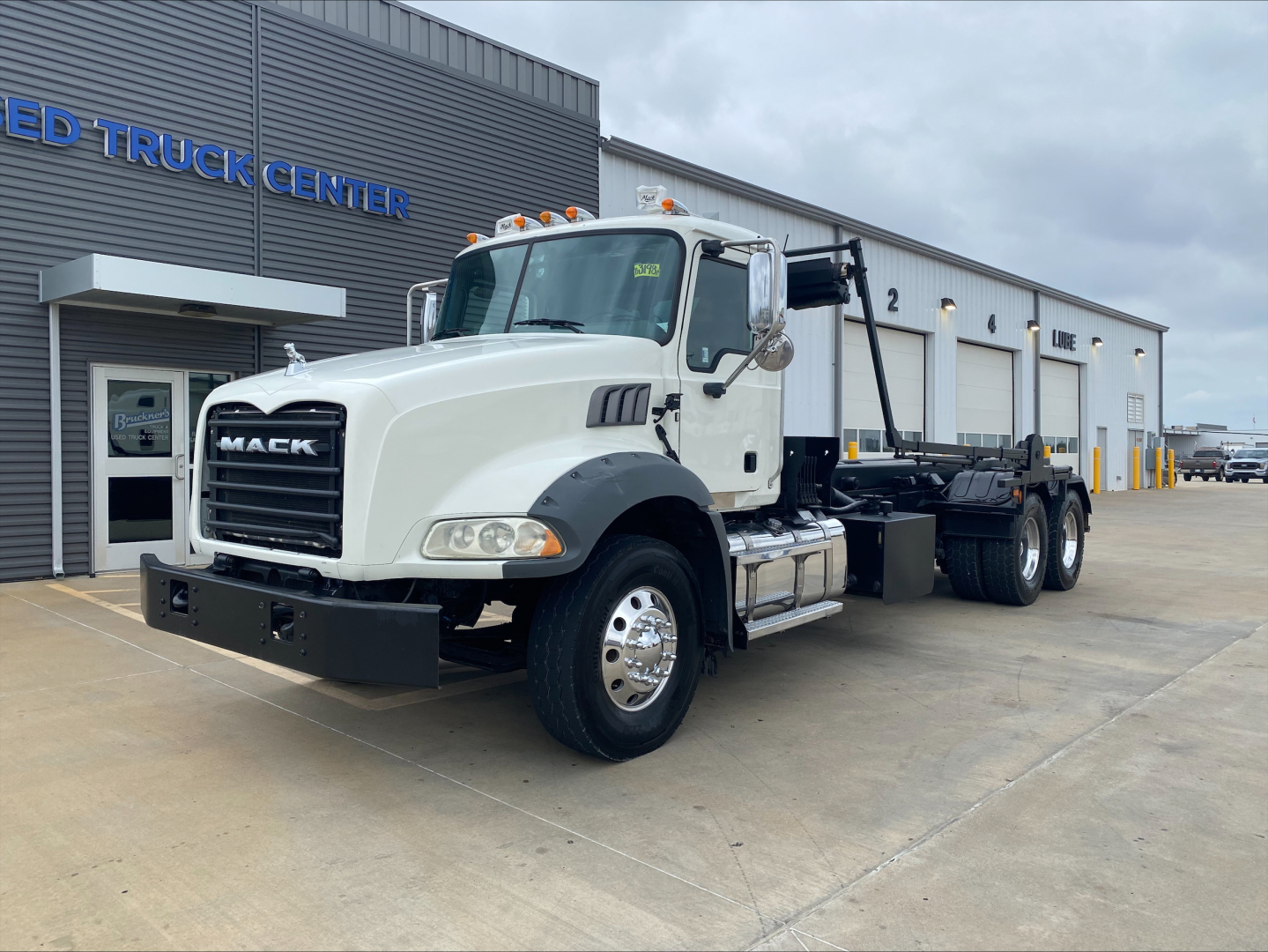 2018 Mack GU533 roll-off truck shown in a dealership lot, white cab with black front bumper and hoist mechanism; Mack emblem on grille.