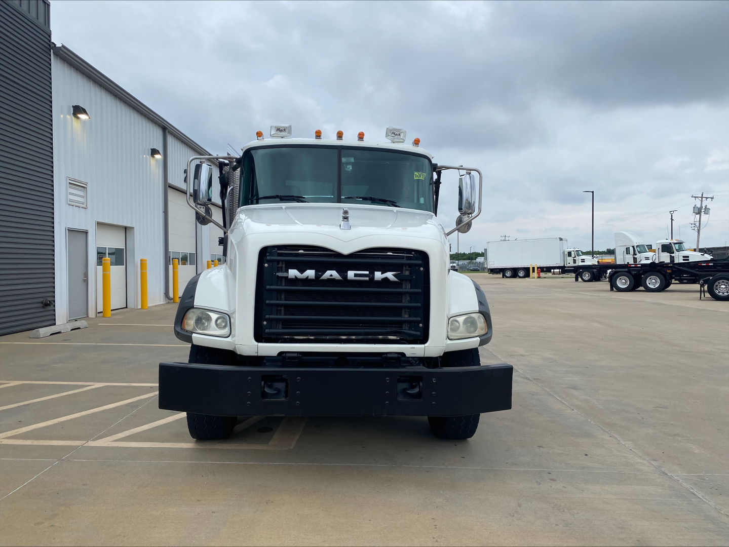Front view of a white 2018 Mack GU533 roll-off truck showing large black grille with MACK lettering, bumper, and cab mirrors.
