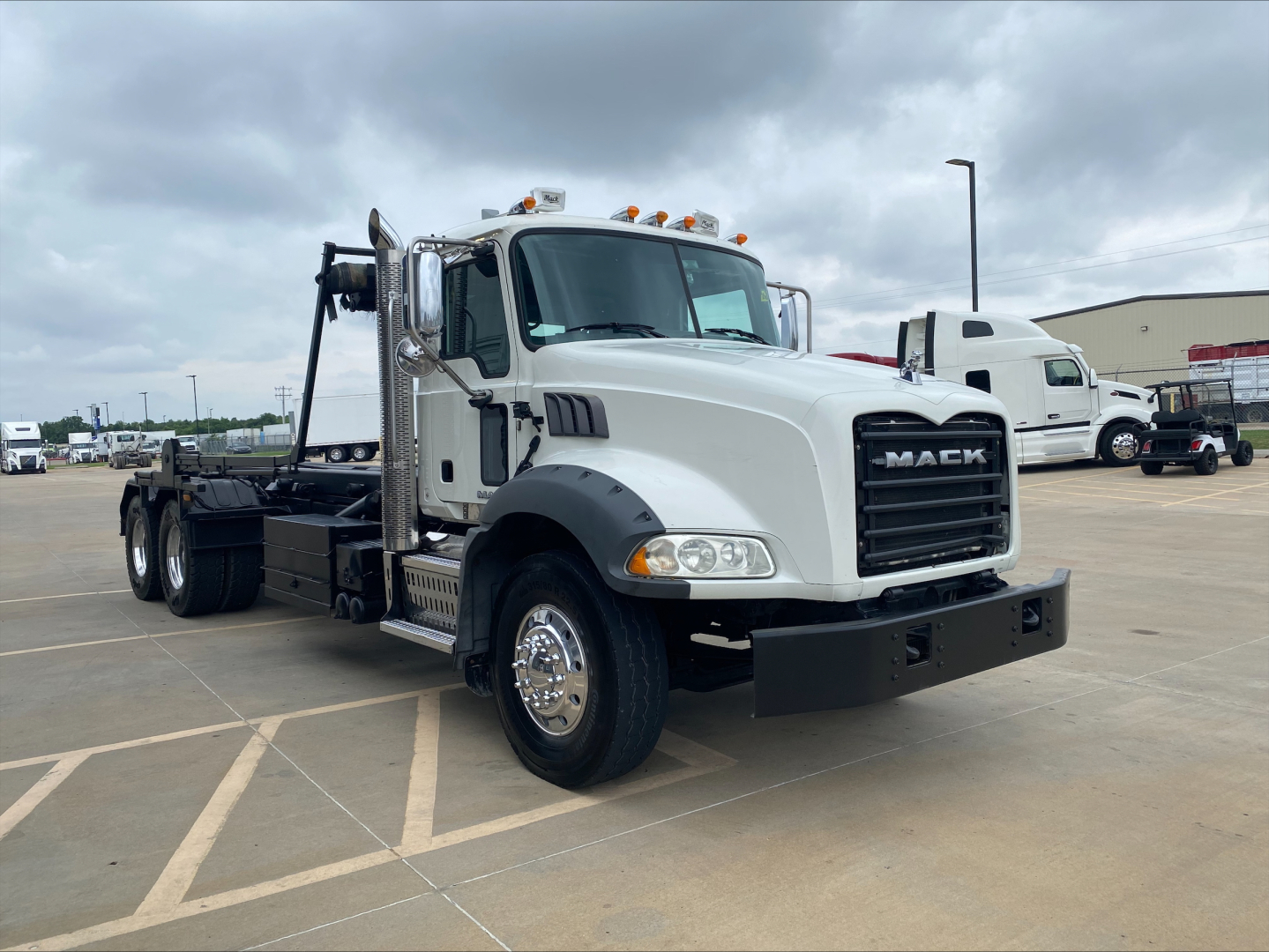 2018 Mack GU533 rolloff truck with cab and chassis, front grille with MACK branding, chrome front bumper, large side mirrors, amber clearance lights on cab roof, and a hydraulic roll-off hoist.