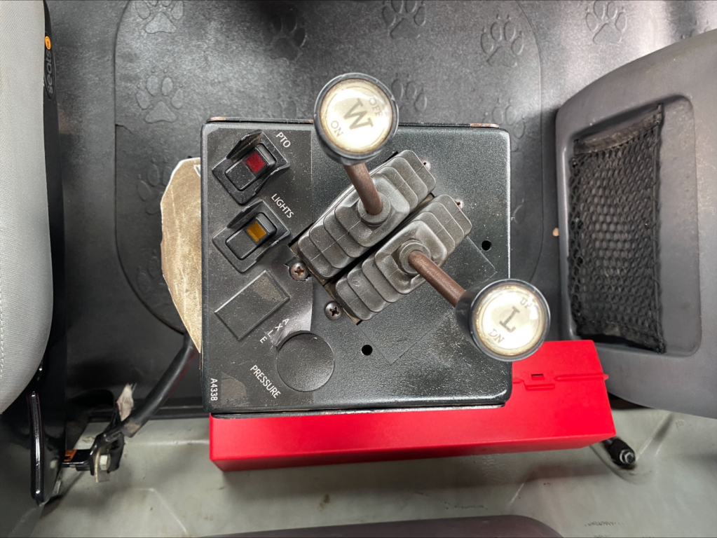 Dash control panel with two levers and switches in a Mack GU533 roll-off truck, showing label text on levers and surrounding dashboard area.
