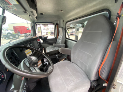 Cab interior of 2018 Mack GU533 roll-off truck showing steering wheel and dashboard, gray cloth seats, and left-side driver seat in view.
