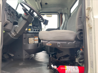 Truck cab interior of a 2018 Mack GU533 roll-off with steering wheel, dashboard, driver seat, and a red fire extinguisher mounted beneath the seat.