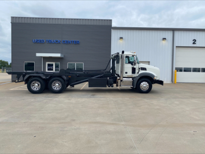 Mack GU533 dump truck side view showing roll-off configuration with extended chassis and hydraulic arms at a used truck center.