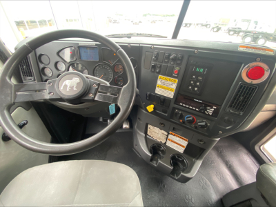 Cab interior of a 2018 Mack GU533 roll-off truck showing steering wheel, dashboard gauges, controls, and a yellow caution label.